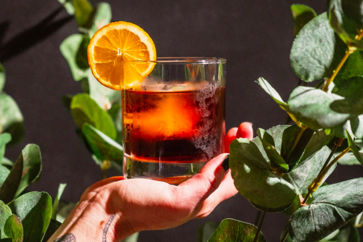 hand holding a cocktail in a glass with an orange slice on the rim